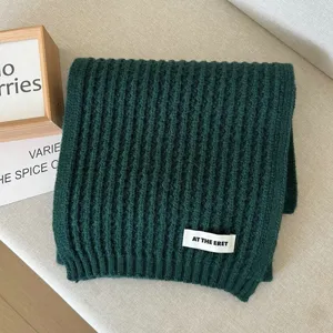 Detailed shot of a dark green ribbed knit winter scarf with a stylish brand label.