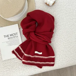 Detailed shot of a cozy red knitted wool scarf with white striped hem on fluffy background.