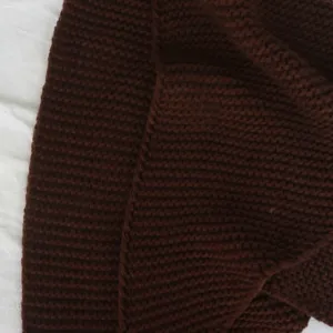 Close-up detail van een donkerbruine gebreide driehoekige sjaal met een fijne, zachte textuur.