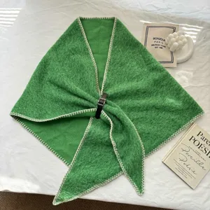 Détail de châle triangulaire en tricot vert avec coutures blanches et boucle en cuir noir.