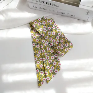 Gros plan sur le détail du petit foulard en soie jaune à fleurs, élégant ruban blanc.