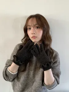 Detailed close-up shot of dark grey knit gloves featuring cute ruffle cuffs, cozy texture.