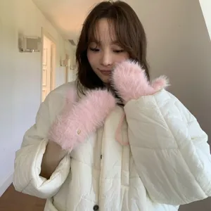 Close-up detail of soft fluffy pink winter mittens worn by a model in a cozy indoor setting.