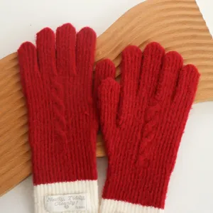 Close-up detail of winter red knit gloves with white cuffs and decorative fabric label.