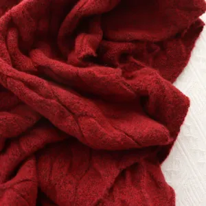 Detail view of a cozy deep red knitted cable shawl, soft winter scarf fabric texture.