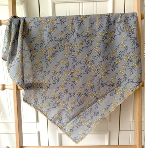 Vue de détail d'un carré de coton gris à fleurs jaunes et bordure en dentelle délicate.
