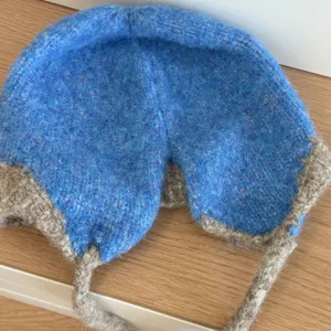 Detalle en primer plano del gorro de punto mullido, con orejeras cálidas y tiras prácticas.