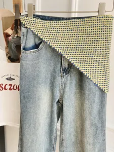 Asymmetric denim jeans with attached yellow blue knit scarf waist wrap trendy fashion detail shot.