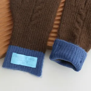 Close-up detail of knitted gloves featuring brown and blue contrasting cuffs with a cute tag.