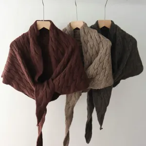 Detailed view of solid color cable knit shawl and triangular scarf hanging on wooden hangers.