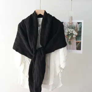 Black cable knit shawl scarf detail hanging on wooden hanger with white blouse background.