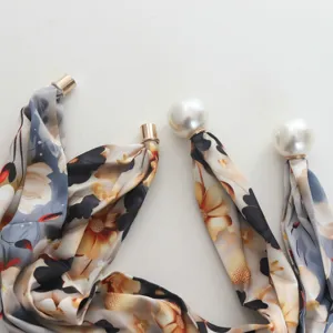 Primo piano di foulard in seta con stampa floreale e fibbia magnetica di perle.