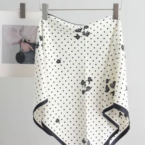 Close-up detail of white triangular scarf with black polka dots and floral pattern display.