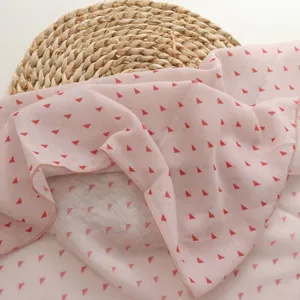Close-up detail view of a soft pink square scarf featuring delicate red geometric triangle print.