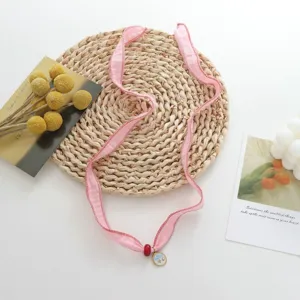 Delicate pink fabric ribbon choker necklace with small pendant and red bead detail.