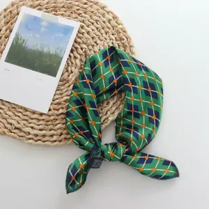 Close-up detail of the green geometric printed silk-like square scarf, showing fabric texture.