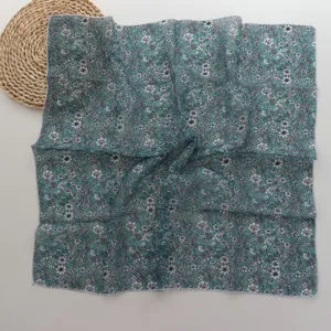 Close-up detail of a dark cyan small square scarf featuring delicate white floral prints, lightweight.