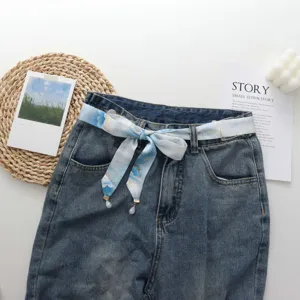 Vue détaillée de jeans bleus assortis à un ruban de soie floral et un pendentif perlé.