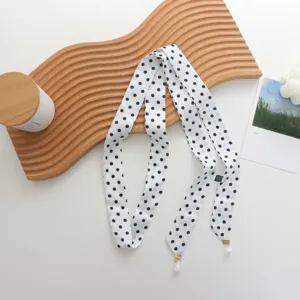 Gros plan d'une écharpe ruban en soie à pois noirs et blancs avec élégant pendentif perle.