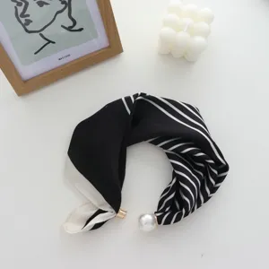 Dettaglio di una sciarpa in seta stretta a righe bianche e nere con chiusura magnetica di perle.