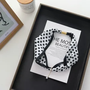 Black and white polka dot silk scarf with magnetic buckle and pearl pendant detail.