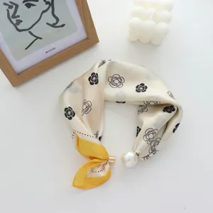 Primo piano della sciarpa in seta stretta con chiusura magnetica di perla e motivo floreale.