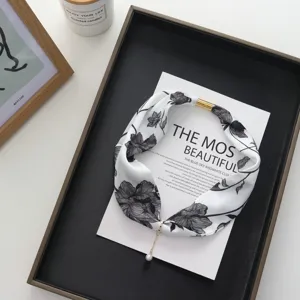 Close-up detail of the elegant black and white floral silk scarf with magnetic buckle.