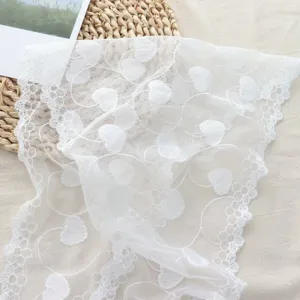 Detailed view of white lace fabric with sweet heart embroidery and delicate scalloped edge.