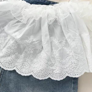 Dettaglio gonna con volant in pizzo bianco, ricamo floreale traforato, accessorio a strati.