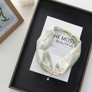 Detail close up shot of a floral print silk scarf with magnetic buckle and pearl pendant.