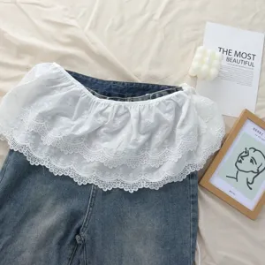 Gonna grembiule in pizzo bianco con volant elegante abbinata a pantaloni in denim blu.
