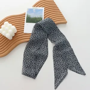 Detail view of a chic black and grey long ribbon scarf styled with minimalist wooden tray.