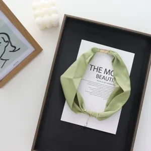 Detail shot of lightweight green silk scarf with magnetic clasp and pearl pendant for women.