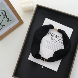 Black fabric neckerchief detail with gold rings and pearl pendant in elegant flat lay.