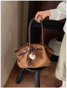 Detail van bruine suède tote tas met zacht materiaal, retro schouderriem en schattige berenhanger.