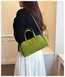 Detailansicht der grünen Wildleder Boston Handtasche mit braunen Flechtkanten und Schultergurt.