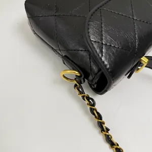 Detail view of black quilted leather crossbody bag with a classic gold chain strap.