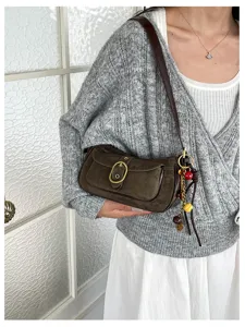 Close-up view of a retro suede shoulder bag featuring a metal buckle and chic charm.