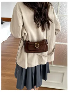 Detail shot of retro brown suede crossbody shoulder bag with metal buckle and flap design.