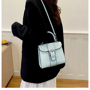 Light blue crocodile textured handbag detail featuring elegant metal buckle and strap.