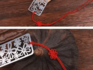 Marque-page en metal evide avec fleurs et gland rouge pour les amateurs de lecture.