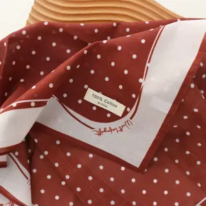 Detail shot of red cotton polka dot scarf with white border and brand label, soft fabric.