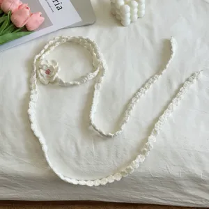 Detailansicht eines weißen handgehäkelten dünnen Schals mit süßem Blumenakzent, Flatlay.