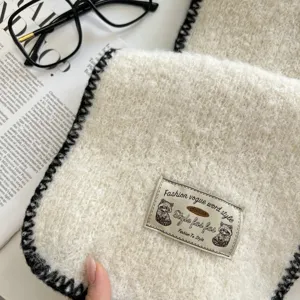 Close-up detail of soft textured knit scarf with chic black contrast whipstitch trim and label.