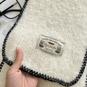 Detailed view of white fuzzy knit scarf with black whipstitch edge and brand label.
