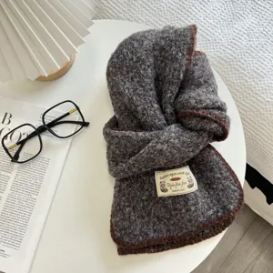 Detail view of cozy textured knit scarf with brown trim and woven label on white table.