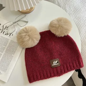 Chic red knitted winter beanie with fluffy dual pom-poms and cute panda patch detail.