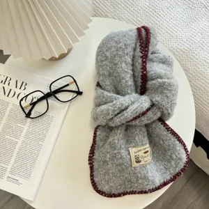 Detailed view of grey bouclé knit scarf with dark red contrast rim and woven label.