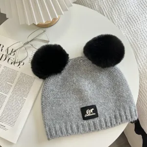 Gray knitted beanie with dual black pom poms and front brand patch, winter warm.