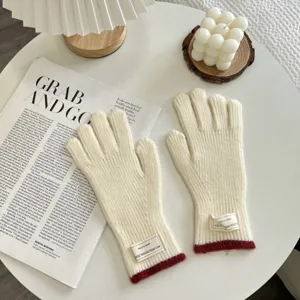 Close-up of winter knitted gloves, beige with red cuffs and small decorative label tag.